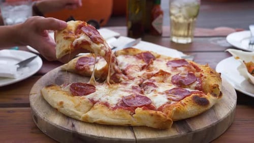 Hand taking sliced pizza. Hot melted cheese is stretching, close-up.
