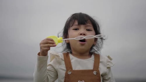 slow motion of happy toddler girl blowing soap bubbles in grass field near the river