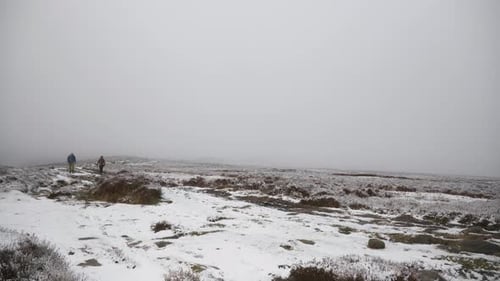 Two people hiking through frozen, snowy fields and moorland.