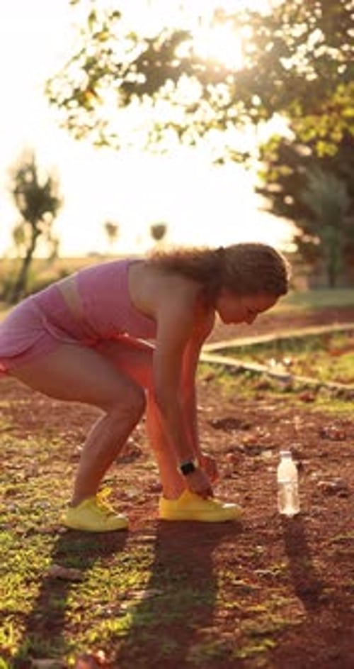Happy young woman runner tying her sport shoes outdoors in autumn park