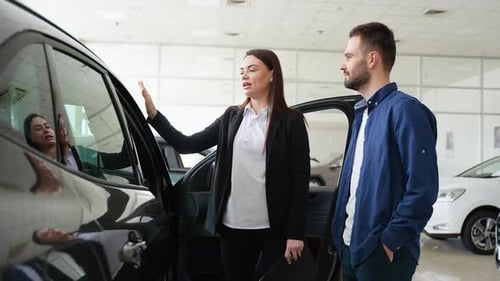 Female Car Dealer Showing New Car to Customer in Showroom