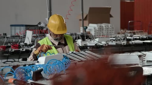 Spécialiste asiatique masculin qui souffle la poussière sur une lampe LED semi-finie lors de l'assemblage