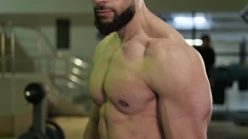 A Handsome Muscular Man with a Beard Poses in the Gym