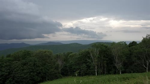 Single-point panoramic shot moving right to left. Cloudy sky over forested mountainous area. Pine tr