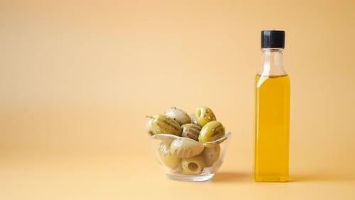 Bottle of Olive Oil and Fresh Olive in a Container on Table