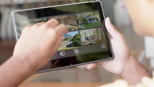 Hands of biracial man using tablet with home security camera views on screen, slow motion