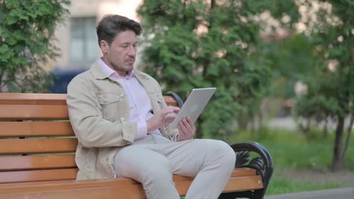 Man Using Tablet Sitting on Park Bench