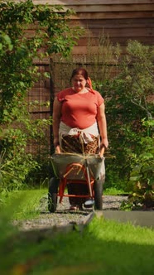 A Woman Confidently Navigates a Garden Path Pushing a Wheelbarrow Filled with Greenery and