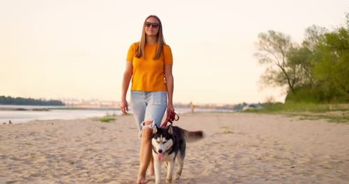 Young Woman Enjoying Evening Walk with Her Pet Dog on the Beach in Summer