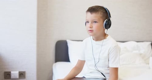 Child Listening with Headphones on Tablet in Bedroom