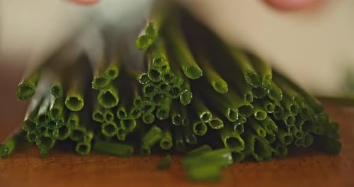 macro shot of a male hand cutting fresh chives on a wooden board
