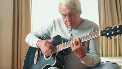 Senior Man Plays Guitar in Bedroom