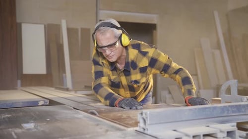 Male carpenter working in carpentry factory cutting boards with saw.