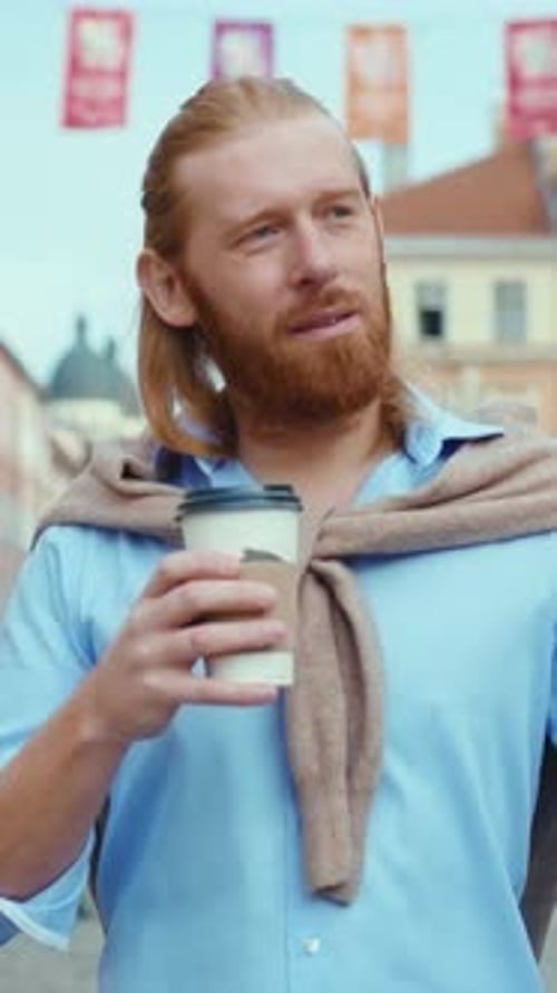 Man With Long Hair Walks in City With Drink