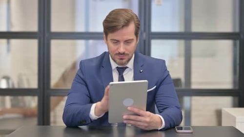 Man in Suit Works With Tablet at Desk