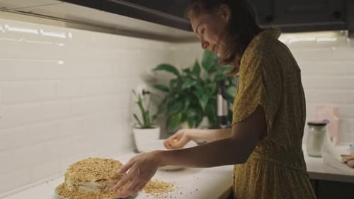 Woman Decorates Layered Cake With Crumb Topping in Kitchen