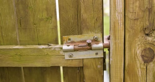Man Unlatching Old Sliding Lock and Opening Gate