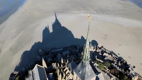 Aerial tilt up shot of showing golden statue on top of famous Mont Saint Michel Church during sunny