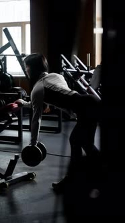Silhouetted Gym Scene with a Focused Female Athlete Lifting a Barbell Fitness Enthusiast Training