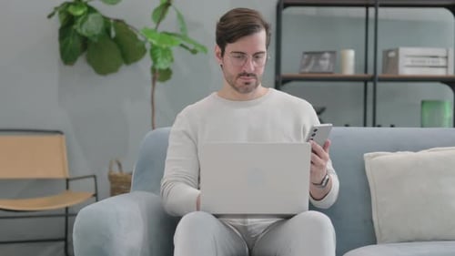 Man Using Laptop and Smartphone on Couch