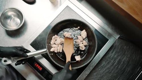 chef in a professional kitchen in a restaurant frying juicy chicken fillet in a frying pan top view