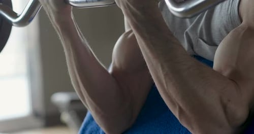 A guy, wearing a tank top in a gym, trains his body to stay fit and have defined muscles. The athl