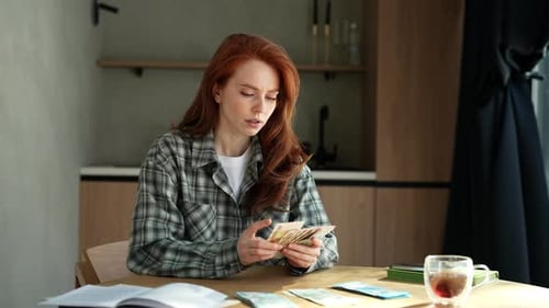 Red Haired Woman Counting Money at Table Indoors