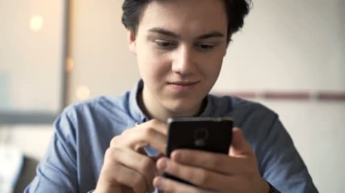Teenager Surfing Internet, Texting On Smartphone In Cafe