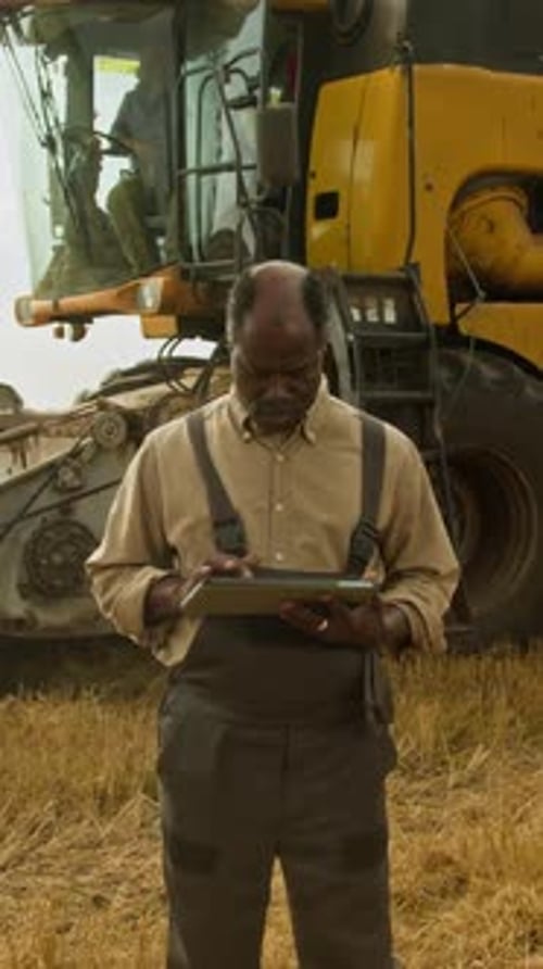 Man Uses Tablet in Front of Combine Harvester