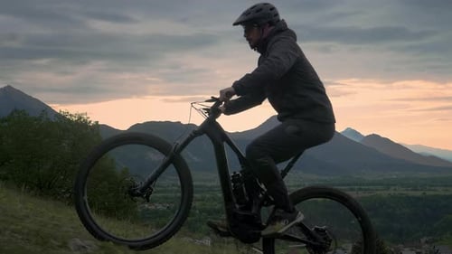 Close up shot of young athletic man on MTB e-bike pedalling up the hill in the morning.