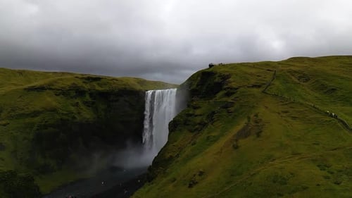 cinematic drone footage of Skógafoss Waterfall in Iceland, capturing the immense curtain of water