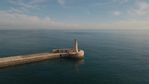 Cinematic aerial shot zooming towards a stone light house at the end of a jetty during a beautiful s