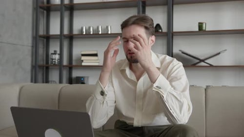 Man Looks Tired While Working at Home on Laptop