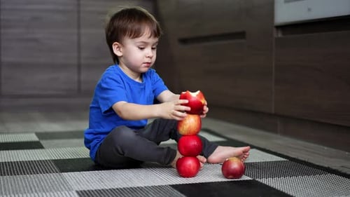 Adorable Caucasian toddler building a tower of red apples.