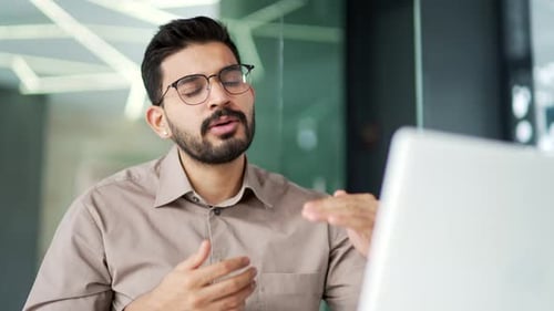 Confident businessman talking on a video call using a laptop sitting at workplace in business office