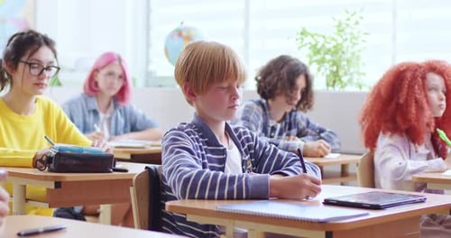 Étudiant masculin concentré étudiant à l'école avec ses camarades de classe Écolier attentionné en vêtements décontractés écrivant