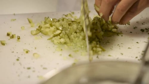Close-up of hands chopping pickles on a white cutting board in a kitchen setting
