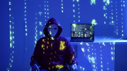 Hacker anonyme en sweat à capuche et masque orange assis avec un ordinateur portable sous les lumières rouges et bleues de la police et Digi
