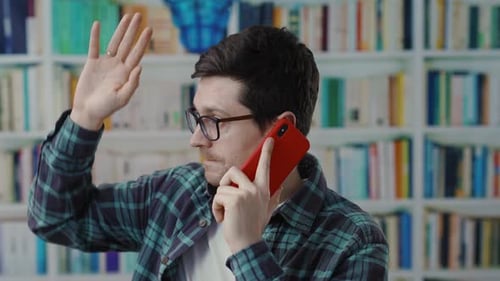 Un jeune homme dans une bibliothèque est profondément engagé dans une conversation téléphonique