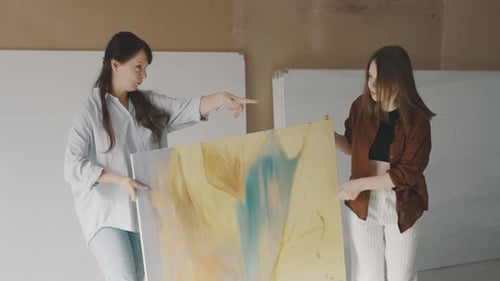 Artistic collaboration between two women showcasing a colorful painting in a studio setting