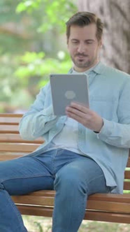 Young Man using Tablet while Sitting Outdoor on a Bench, vertical video