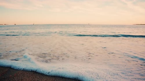 Nahaufnahme kleiner Meereswellen, die bei Sonnenuntergang sanft auf den Sandstrand rollen