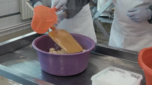 Hands of Cheesemakers Pouring Hot Water over Cooked Curd in Plastic Tub