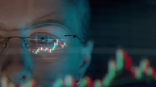 Un trader portant des lunettes travaille sur un écran d'ordinateur portable avec des graphiques boursiers et Bitcoin BTC