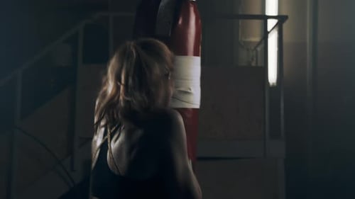 Woman fighter throws fast and hard punches on a punching bag while practicing at home in her garage.
