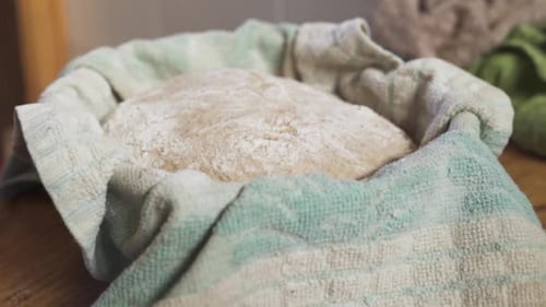 Bread Dough Resting In A Basket Covered In Towel On Top Of A Wooden table. - slow mo - backward shot