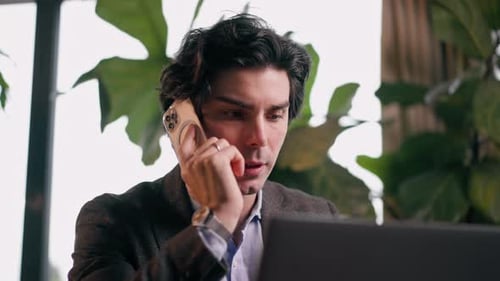 a serious man a businessman works at a laptop in the office communicates with colleagues smartphone