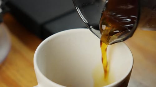 Pouring Fresh Black Coffee From Glass Pot Into White Cup In Kitchen, Close Up