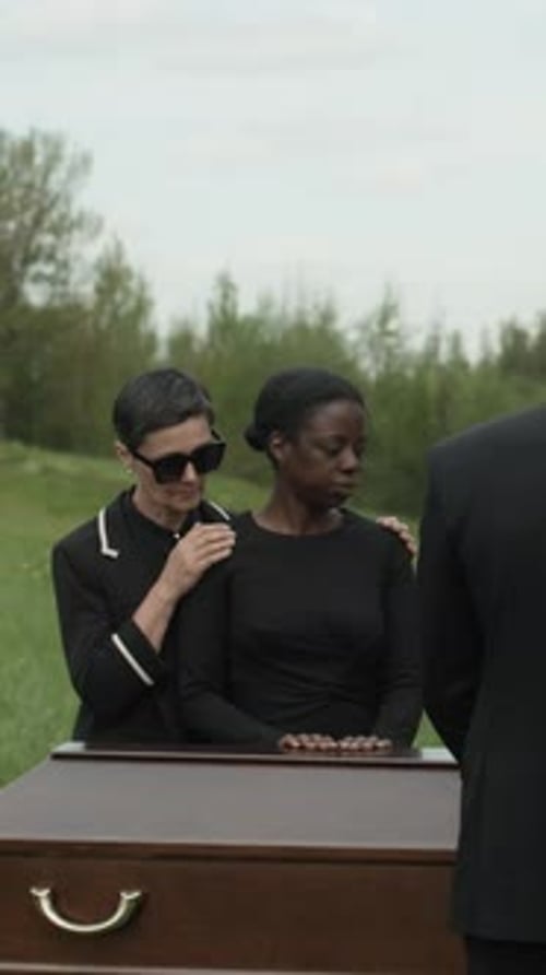People Mourning Beside Coffin in Grassy Field