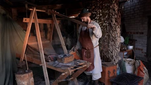 A working blacksmith. Media. An adult man who works with iron and fire with wooden equipment.